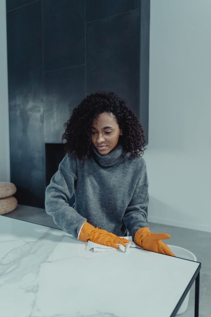 A woman wearing gloves cleans a marble table in a modern indoor setting, focusing on cleanliness and hygiene.